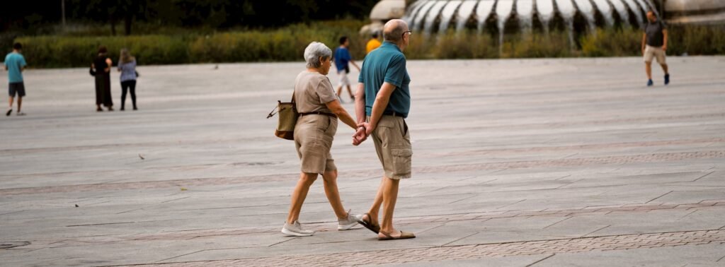 An older couple holding hands while walking across a plaza