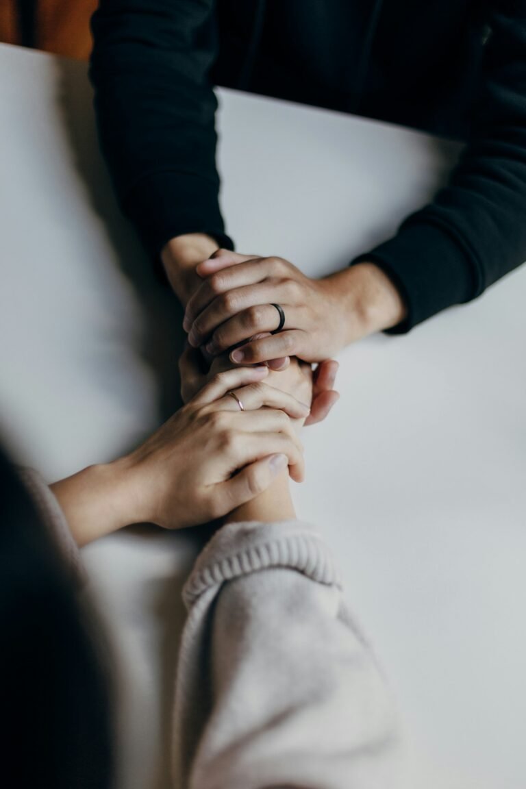 Two people sitting at a table with their hands clasped together, one comforting the other.