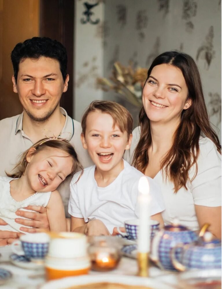 A family of four smiling together at a table set for tea