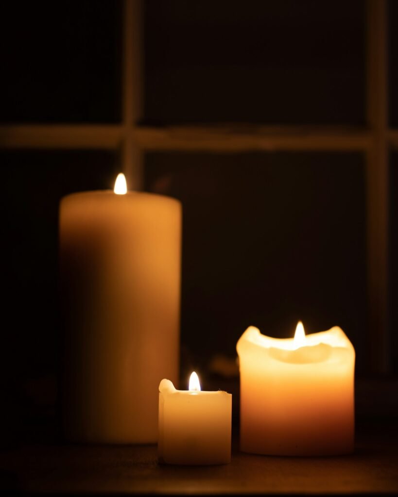 Three lit candles on a table in front of a window
